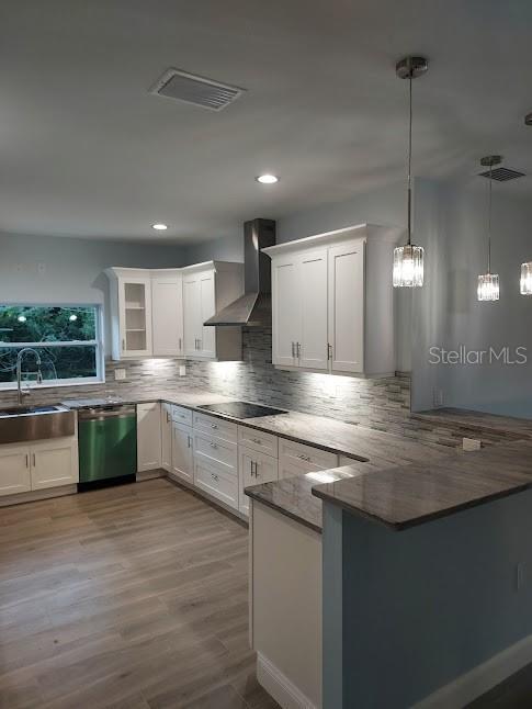 kitchen with stainless steel dishwasher, sink, kitchen peninsula, wall chimney range hood, and white cabinetry