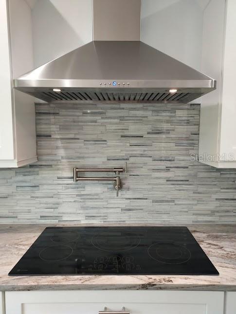 room details with wall chimney range hood, white cabinets, backsplash, and black electric stovetop