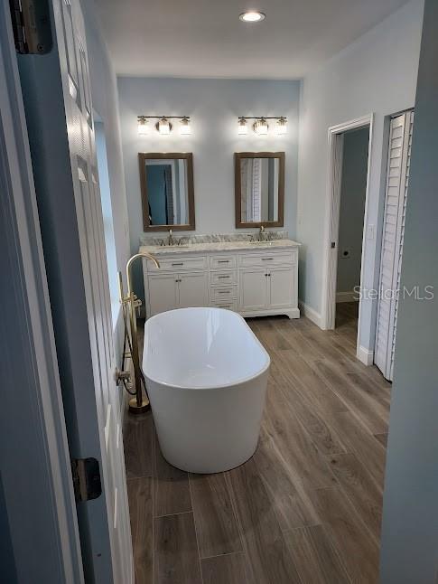 bathroom with wood-type flooring, a tub to relax in, and vanity