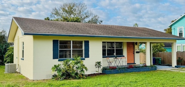 view of front of property featuring central AC unit, concrete block siding, roof with shingles, fence, and a front yard