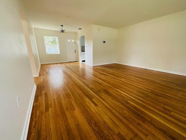 empty room with arched walkways, baseboards, and wood finished floors