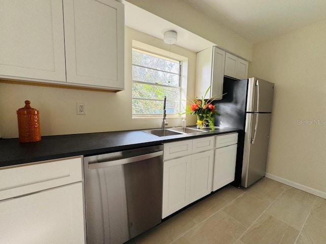 kitchen with appliances with stainless steel finishes, dark countertops, white cabinets, and a sink