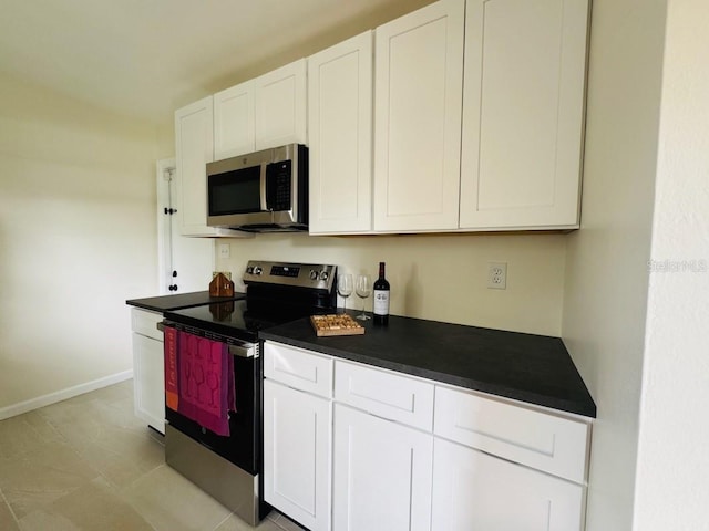 kitchen with dark countertops, baseboards, appliances with stainless steel finishes, and white cabinets