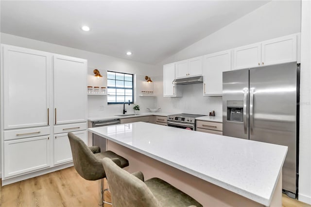 kitchen featuring a kitchen breakfast bar, white cabinets, appliances with stainless steel finishes, and vaulted ceiling