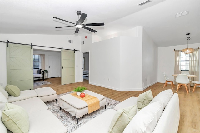 living room featuring lofted ceiling, wood-type flooring, a barn door, and ceiling fan