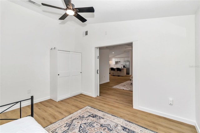 bedroom with ceiling fan, a closet, lofted ceiling, stainless steel fridge with ice dispenser, and hardwood / wood-style flooring