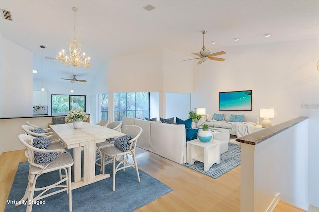 dining space featuring high vaulted ceiling, light hardwood / wood-style flooring, and ceiling fan with notable chandelier