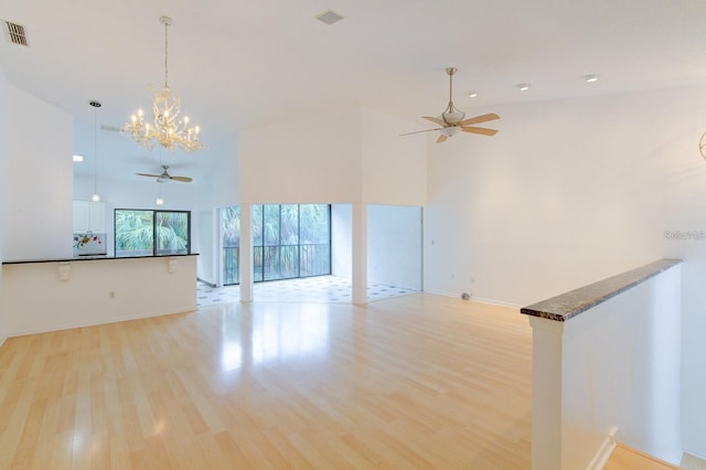 unfurnished living room featuring a towering ceiling, ceiling fan with notable chandelier, and light hardwood / wood-style flooring