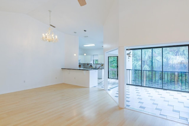 unfurnished living room featuring high vaulted ceiling, a chandelier, and light hardwood / wood-style flooring