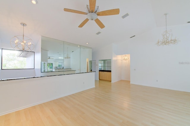 unfurnished living room featuring ceiling fan with notable chandelier, light hardwood / wood-style flooring, and vaulted ceiling