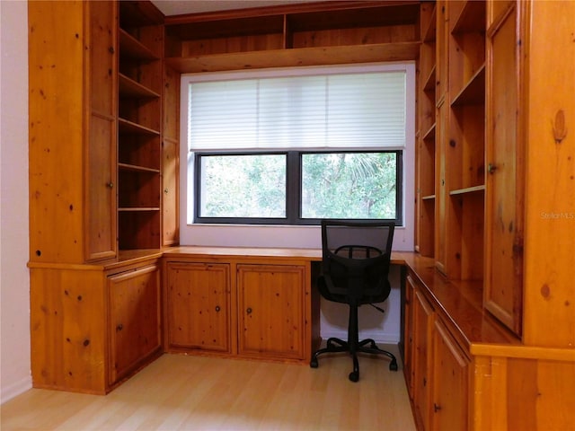 unfurnished office featuring a wealth of natural light, built in desk, and light hardwood / wood-style floors