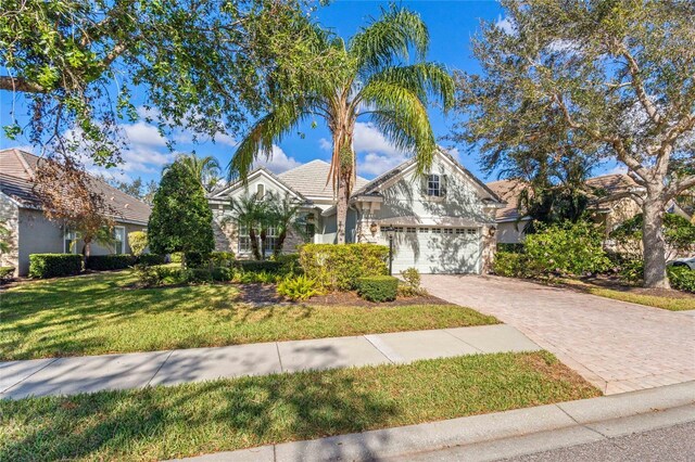 12121 Thornhill Ct, Lakewood Ranch, FL 34202 - view of front of house with stucco siding, decorative driveway, a front yard, stone siding, and an attached garage