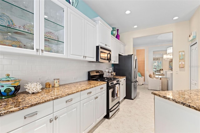 kitchen featuring appliances with stainless steel finishes, backsplash, light stone counters, white cabinets, and a chandelier