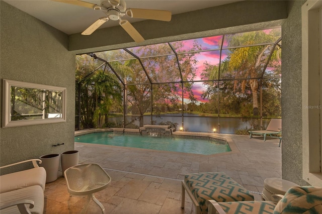 pool at dusk with a lanai, ceiling fan, pool water feature, and a patio