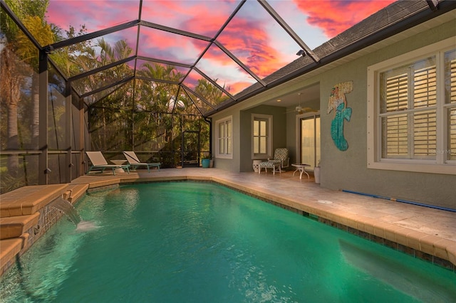 pool at dusk with pool water feature, ceiling fan, a lanai, and a patio