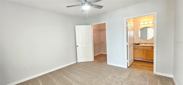 unfurnished bedroom featuring a walk in closet, connected bathroom, a closet, ceiling fan, and light colored carpet