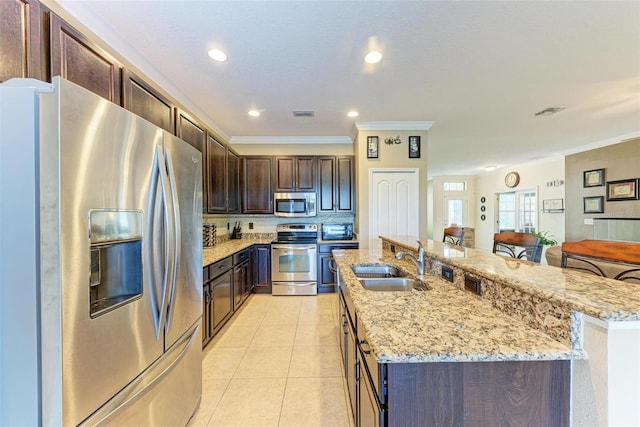 kitchen with sink, dark brown cabinets, stainless steel appliances, ornamental molding, and a center island with sink