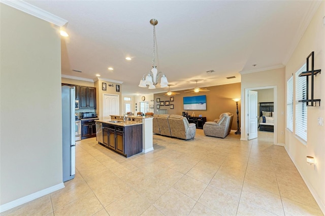 kitchen with light tile patterned flooring, dark brown cabinetry, light stone counters, ornamental molding, and a kitchen island with sink