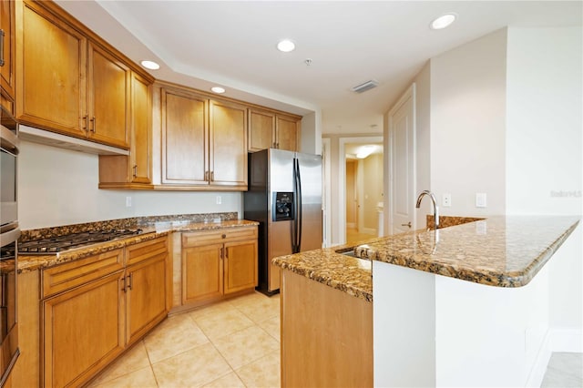 kitchen with stone countertops, kitchen peninsula, stainless steel appliances, sink, and light tile patterned floors