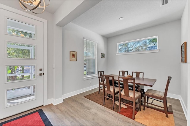 dining room with plenty of natural light, wood-type flooring, a textured ceiling, and an inviting chandelier