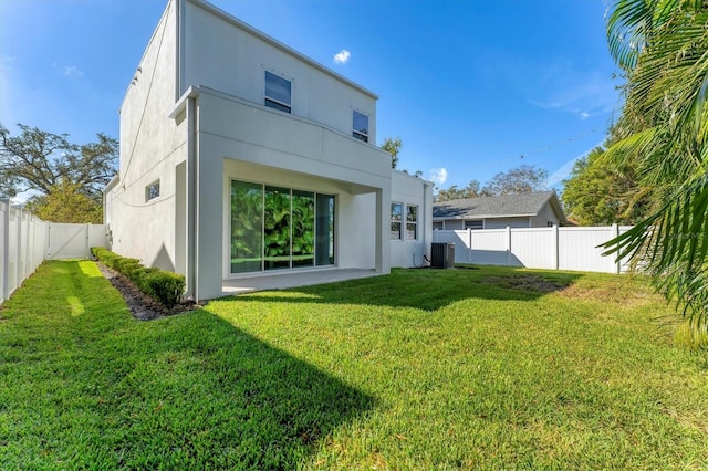 rear view of house featuring a yard, central AC unit, a fenced backyard, and stucco siding