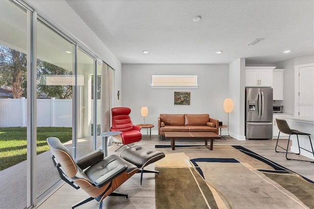 living room with a wall unit AC, baseboards, visible vents, recessed lighting, and a textured ceiling