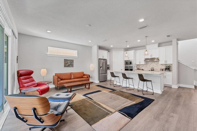 living room featuring light wood-type flooring, visible vents, baseboards, and recessed lighting