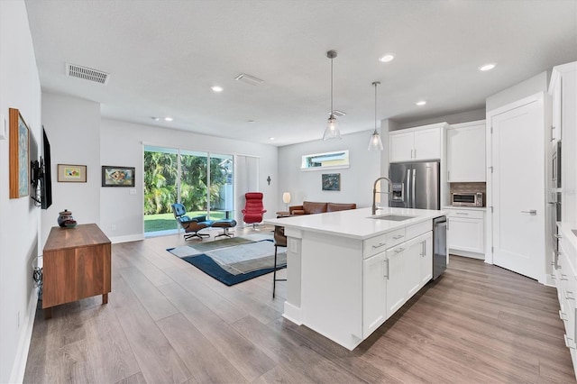 kitchen featuring pendant lighting, white cabinets, an island with sink, tasteful backsplash, and stainless steel appliances