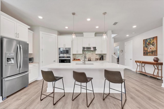 kitchen featuring tasteful backsplash, under cabinet range hood, light countertops, appliances with stainless steel finishes, and a sink