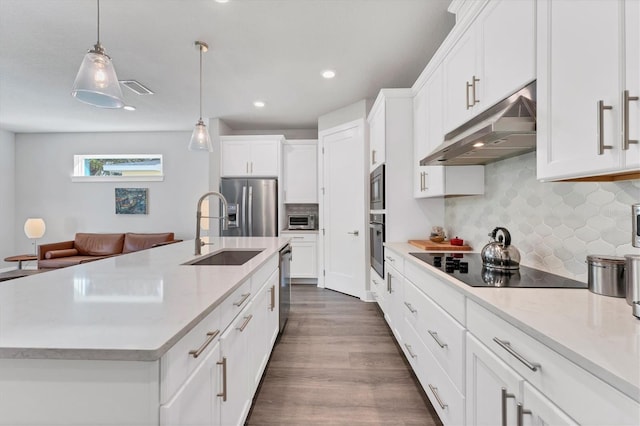 kitchen featuring sink, stainless steel appliances, an island with sink, decorative light fixtures, and white cabinets