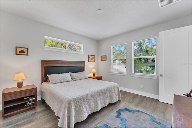 bedroom featuring baseboards, multiple windows, visible vents, and wood finished floors