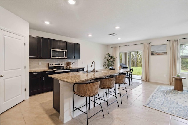 kitchen featuring a healthy amount of sunlight, stainless steel appliances, a breakfast bar area, and an island with sink