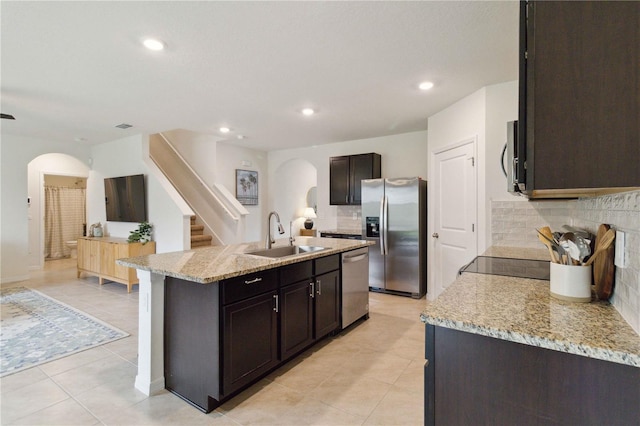 kitchen with backsplash, a center island with sink, sink, light stone countertops, and appliances with stainless steel finishes