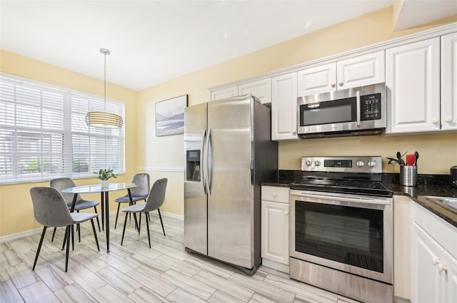 kitchen featuring light wood-type flooring, appliances with stainless steel finishes, decorative light fixtures, and white cabinetry