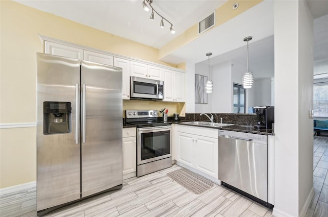 kitchen with appliances with stainless steel finishes, white cabinetry, sink, and hanging light fixtures