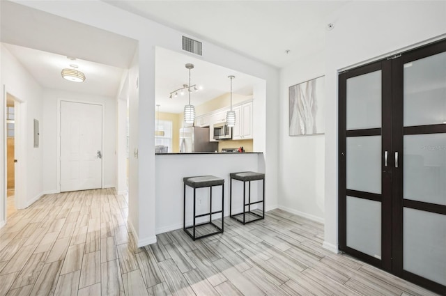 kitchen featuring white cabinets, appliances with stainless steel finishes, a kitchen breakfast bar, light hardwood / wood-style flooring, and pendant lighting