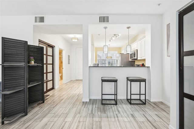 kitchen featuring appliances with stainless steel finishes, a breakfast bar area, white cabinetry, pendant lighting, and light hardwood / wood-style flooring