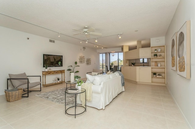 living room with ceiling fan, a textured ceiling, rail lighting, and light tile patterned floors