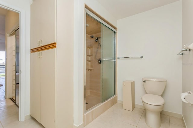 bathroom with a shower with door, tile patterned floors, and toilet