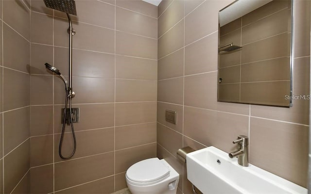 bathroom with a sink, a tile shower, toilet, and tile walls