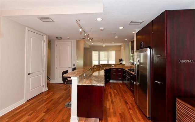 kitchen with kitchen peninsula, dark hardwood / wood-style flooring, a kitchen bar, and stainless steel fridge