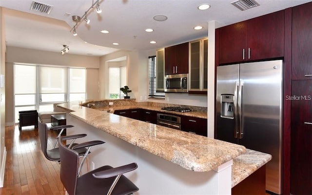 kitchen featuring a kitchen island, a kitchen bar, light wood-type flooring, stainless steel appliances, and light stone counters