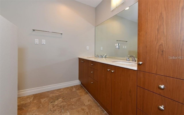 bathroom with double vanity, baseboards, stone finish floor, and a sink
