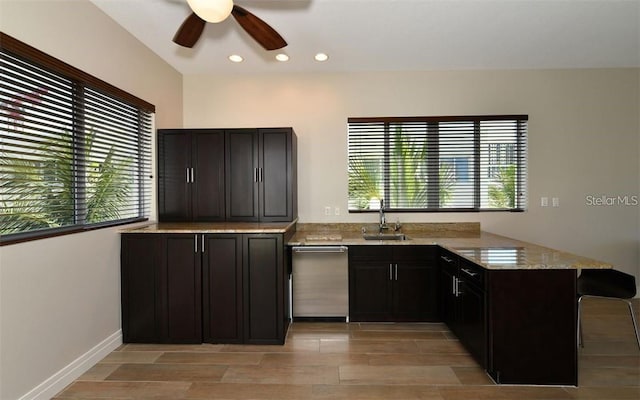 kitchen with a ceiling fan, stainless steel dishwasher, light stone countertops, a sink, and a peninsula