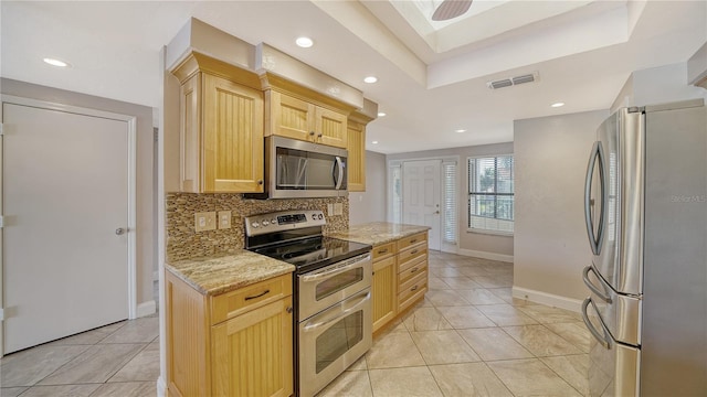 kitchen with decorative backsplash, light brown cabinets, appliances with stainless steel finishes, light stone counters, and a skylight