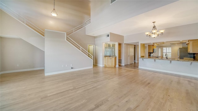 unfurnished living room featuring a notable chandelier, a towering ceiling, and light hardwood / wood-style flooring