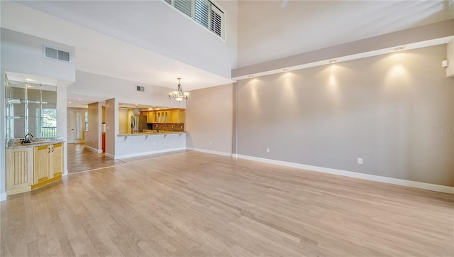 unfurnished living room with a towering ceiling, a notable chandelier, sink, and light wood-type flooring