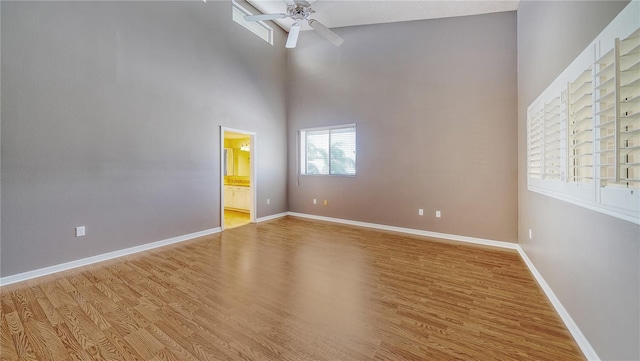 empty room with a high ceiling, a textured ceiling, light wood-type flooring, and ceiling fan