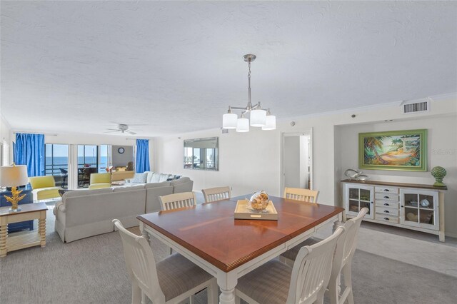 carpeted dining space with a textured ceiling, a water view, ceiling fan with notable chandelier, and ornamental molding