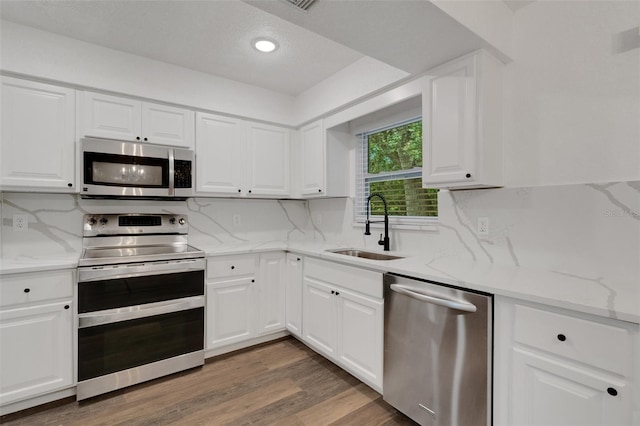 kitchen with dark wood-type flooring, stainless steel appliances, sink, white cabinetry, and tasteful backsplash